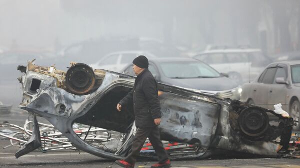 Мужчина проходит мимо машины, сгоревшей во время акций протеста в Алматы. - Sputnik Қазақстан