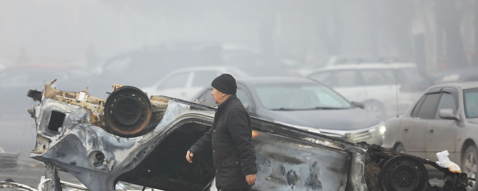 Мужчина проходит мимо машины, сгоревшей во время акций протеста в Алматы. - Sputnik Қазақстан, 1920, 07.01.2022