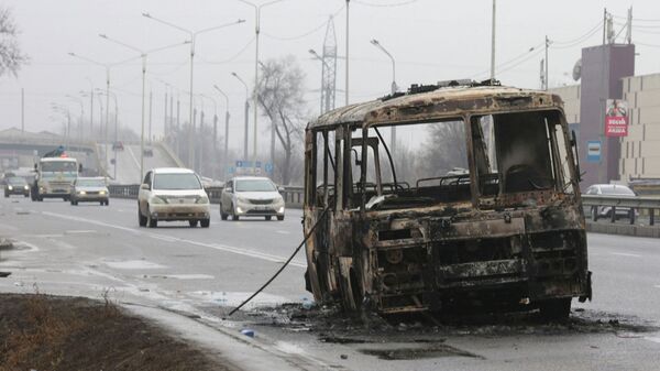 Машины двигаются по улице, на которой стоит разбитый и сожженный автобус - Sputnik Казахстан