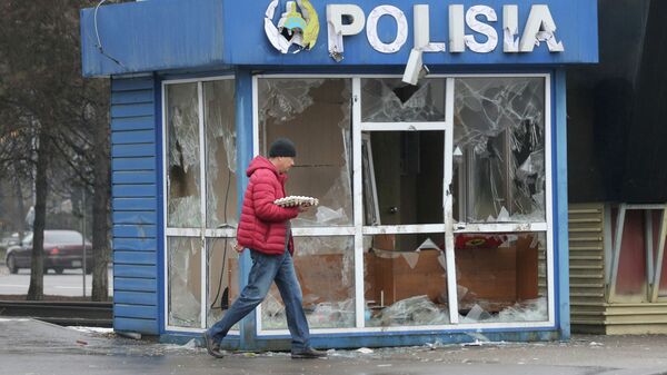 Мужчина проходит мимо разбитого полицейского поста в Алматы  - Sputnik Казахстан