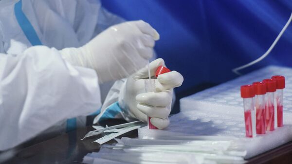 Медик в защитном костюме держит в руках пробирку с пробой для ПЦР теста на коронавирус  - Sputnik Казахстан
