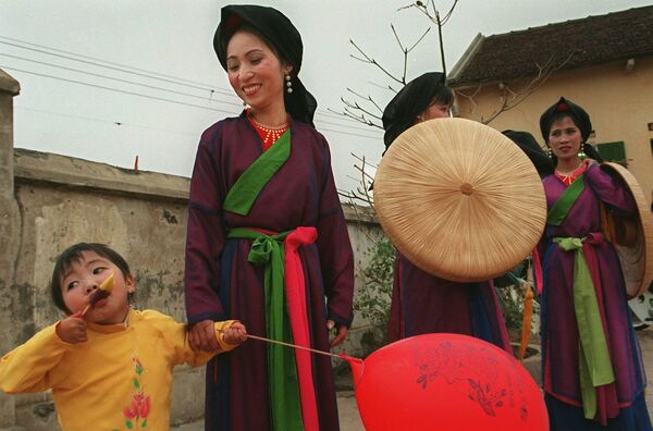 Девочка лакомится мороженым рядом с артистами в традиционных костюмах, исполняющими песни во вьетнамском стиле &quot;Куан хо&quot; в провинции Бакнинь, 10 февраля 1998 года.   - Sputnik Казахстан