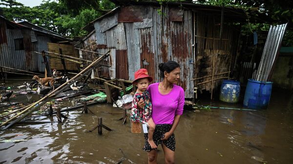 Женщина с ребенком на руках пробирается через паводковые воды на окраине Янгона, Мьянма - Sputnik Казахстан