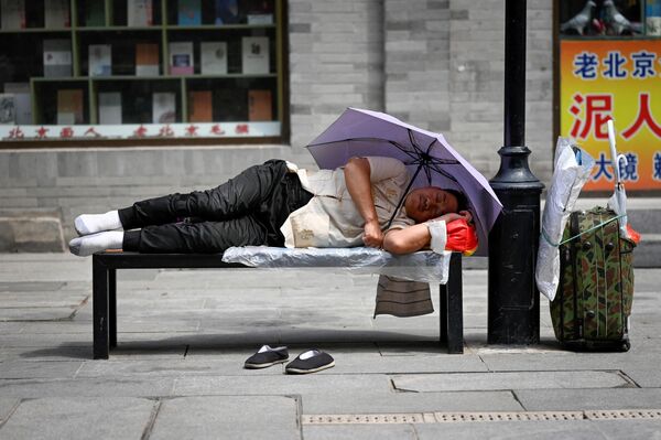 Мужчина отдыхает на скамейке под зонтиком на дороге в Пекине.  - Sputnik Казахстан