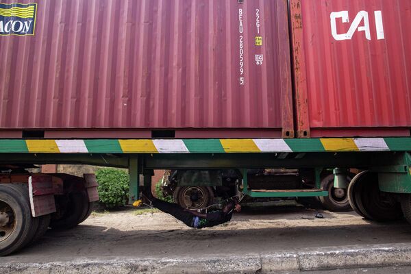 Водитель спит под своим грузовиком, припаркованным на обочине дороги в ожидании доступа в порт Тинкан в Апапе, Лагос, Нигерия.  - Sputnik Казахстан