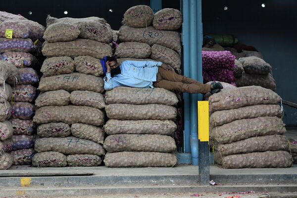 Рабочий в маске спит на мешках с луком на оптовом рынке Азадпур Манди в Нью-Дели.  - Sputnik Казахстан