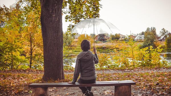 Ребенок на скамейке в осеннем парке под зонтом  - Sputnik Қазақстан