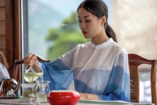 Китайская чайная церемония –это особая философия и культура, зародившаяся в древние времена. Китайцы не просто не спеша пьют чай, а наслаждаются им, вдыхая его аромат, ощущая вкус и изменение цвета напитка в процессе его настаивания. На фото: женщина наливает чай Синьян Маоцзянь во время церемонии открытия церемонии &quot;Наблюдение за горой Даби с высоты 600 000 метров с неба&quot; ,провинция Хэнань, Китай.  - Sputnik Казахстан