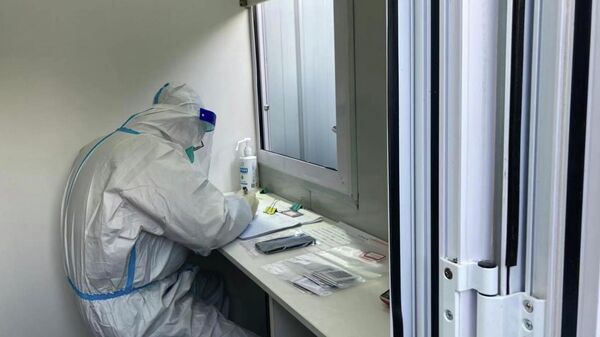 Медик в защитном костюме работает в лаборатории с пробами ПЦР-тестов на коронавирус - Sputnik Казахстан