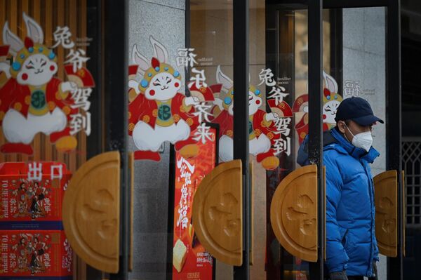 Праздничные и выходные дни в Китае продлятся до 27 января. На фото: мужчина выходит из магазина, украшенного фигурками кролика - символа Нового Года по восточному календарю, в Пекине.  - Sputnik Казахстан