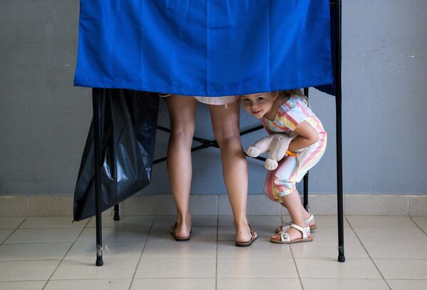 Девочка выглядывает из кабины для голосования на избирательном участке во время всеобщих выборов в Афинах, Греция.  - Sputnik Казахстан