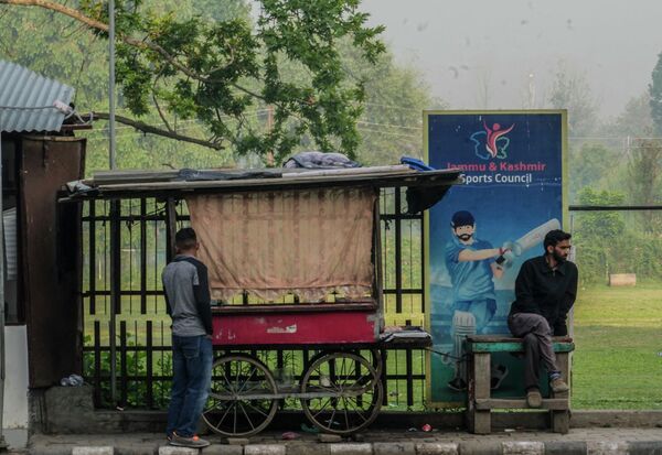 Мужчина из Кашмира сидит возле автобусного вокзала на фоне спортивного плаката в Индии.  - Sputnik Казахстан