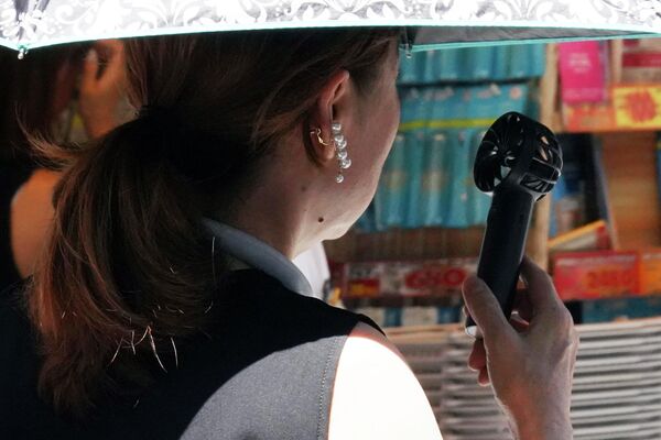 Девушка охлаждается с помощью портативного вентилятора на улице в Токио. - Sputnik Казахстан