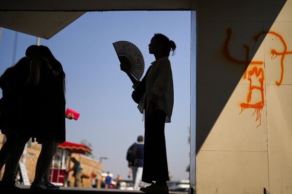 Женщина обмахивает себя веером, стоя в тени под Галатским мостом жарким летним днем в Стамбуле. - Sputnik Казахстан