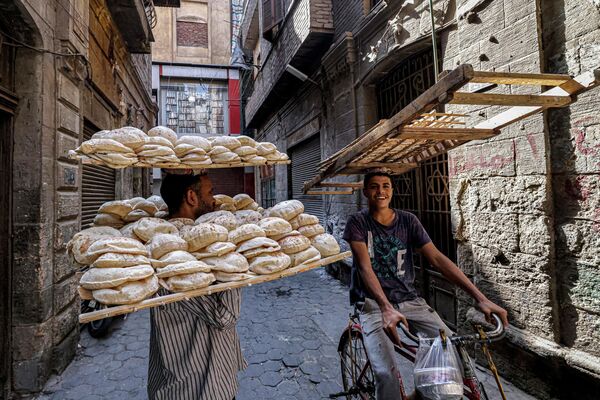 Разносчик готовится передать доставщику на велосипеде лотки со свежим традиционным египетским хлебом из пекарни в Каире, Египет.  - Sputnik Казахстан