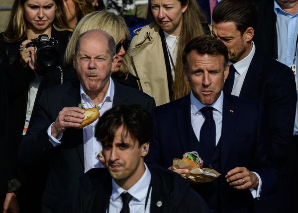 Канцлер Германии Олаф Шольц (слева) и президент Франции Эммануэль Макрон едят бутерброд с рыбой на пирсе в Гамбурге, Германия. - Sputnik Казахстан