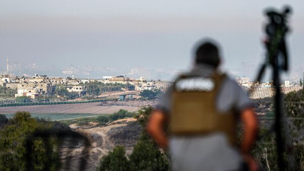 Журналист сидит с камерой и наблюдает с позиции в южно-израильском городе Сдерот за горизонтом северной части сектора Газа во время израильской бомбардировки - Sputnik Қазақстан