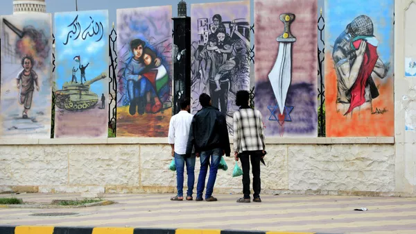 Мужчины смотрят на граффити в знак солидарности с палестинцами сектора Газа и Западного берега, нарисованное на стене мечети на площади Сабин в Сане - Sputnik Казахстан