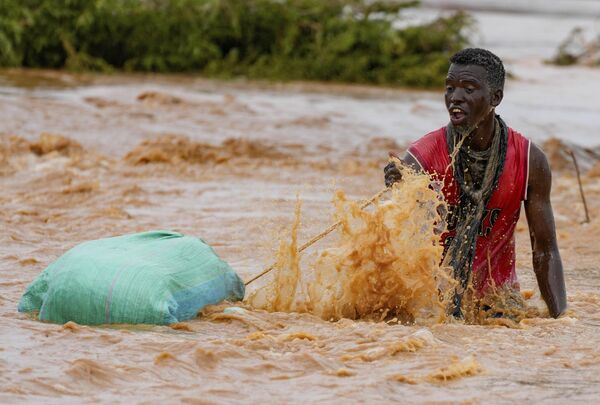 В феврале 2023 года наводнения унесли жизни 2 156 человек в 14 странах Африки. На фото: мужчина тащит свой багаж, пытаясь перейти дорогу, пострадавшую из-за наводнения в результате проливных дождей, Кения, 25 ноября 2023 года. - Sputnik Казахстан