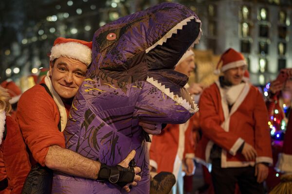 Мужчина в костюме Санта-Клауса обнимает свой надувной костюм динозавра в Лондоне, Великобритания. - Sputnik Казахстан