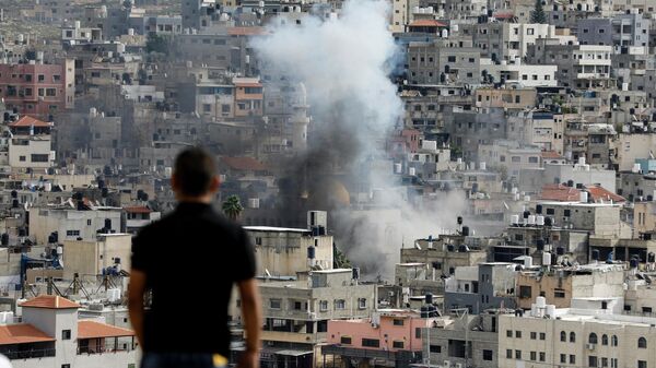 Мужчина наблюдает, как клубы дыма поднимаются над зданиями в лагере палестинских беженцев Нур-Шамс недалеко от оккупированного города Тулькарм на Западном Берегу во время продолжающегося израильского рейда - Sputnik Қазақстан