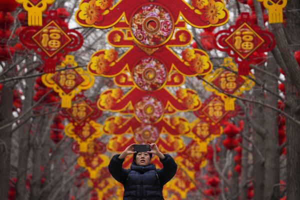 К примеру, в Китае празднование Нового года принято начинать уже накануне с всенародных гуляний. Вечером же все собираются в кругу семьи, накрывают щедрый стол, а утром обмениваются подарками. На фото: женщина фотографирует на смартфон красные фонари и украшения, выставленные вдоль деревьев в преддверии Лунного Нового года в парке Дитан в Пекине. - Sputnik Казахстан