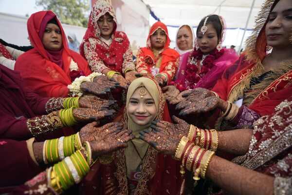 Массовые свадьбы в Индии давно стали традицией и празднуются не первый год.На фото: мусульманские невесты с намазанными хной руками окружают другую молодую невесту, позирующую для фотографии во время массовой свадьбы в Ахмадабаде. - Sputnik Казахстан