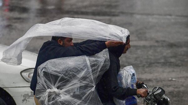 Водители на мотоцикле наматывают на себя полиэтиленовую пленку, чтобы укрыться от дождя, Карачи, Пакистан - Sputnik Казахстан