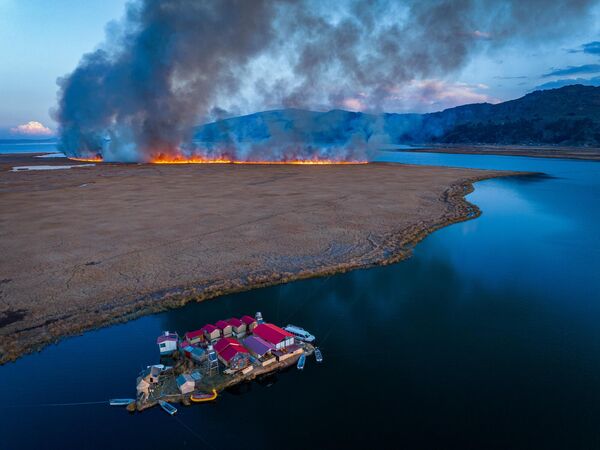 Снимок Яна Ли &quot;Между затишьем и катастрофой&quot;.На озере Титикака, между Перу и Боливией, тихая плавучая деревня резко контрастирует с приближающимся лесным пожаром. - Sputnik Казахстан