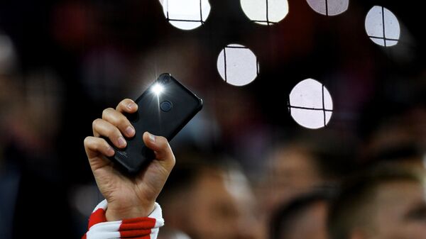 Мобильный телефон с включенным фонариком в руках болельщика  - Sputnik Казахстан