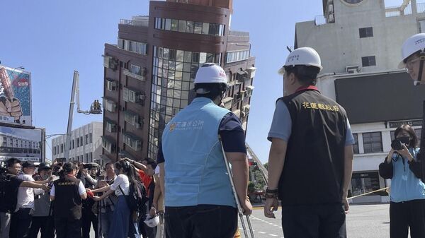 Государственные служащие и журналисты рядом с пожарными, работающими возле наклонившегося здания после землетрясения в Хуаляне, восточный Тайвань, Китай - Sputnik Казахстан