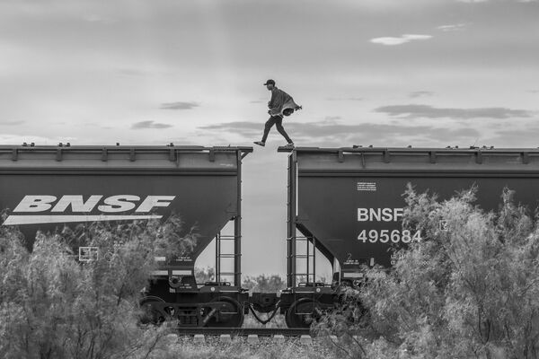 &quot;Две стены&quot;, автор Алехандро Сегарра . На фото: мигрант шагает по вагонам грузового поезда. Как говорится в описании снимка, мигранты, у которых нет финансовых средств, часто прибегают к такому способу передвижения на поездах, чтобы добраться до граница с Соединенными Штатами. Этот вид транспорта очень опасен: за прошедшие годы сотни людей упали на рельсы и погибли или получили увечья.  - Sputnik Казахстан