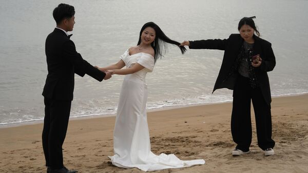 Женщина держит за волосы невесту, делая свадебные фотографии на пляже в Циндао, Китай - Sputnik Казахстан