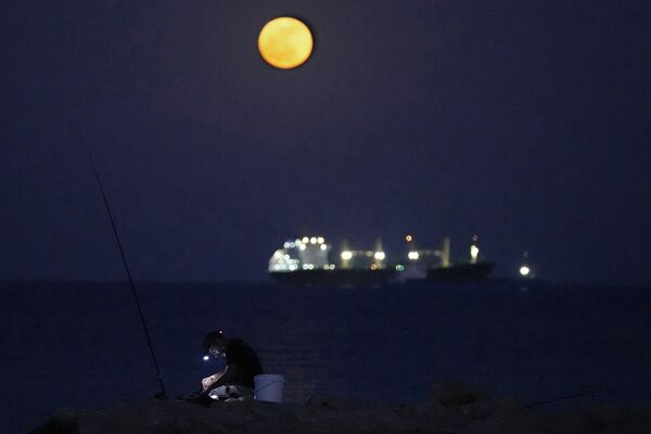 Цветочная полная луна поднимается над кораблем, стоящим на якоре за пределами порта, в южном прибрежном городе Ларнака, на острове Кипр в восточном Средиземноморье. - Sputnik Казахстан