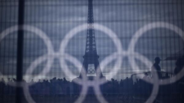 Посетители проходят мимо баннера с олимпийскими кольцами, установленного на ограждении на фоне Эйфелевой башни на площади Трокадеро в Париже, 16 июля 2024 года - Sputnik Казахстан