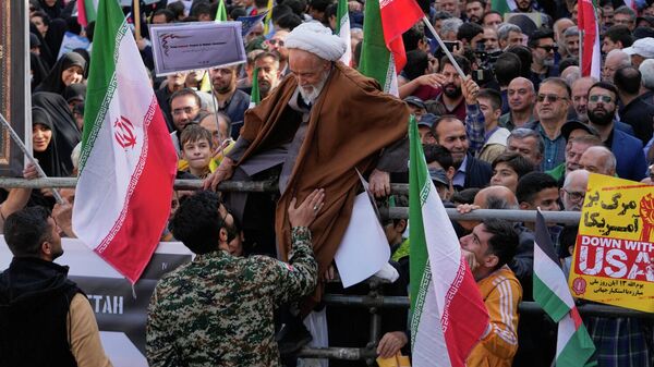 Священнослужитель пытается преодолеть ограждение во время ежегодного митинга перед бывшим посольством США в Тегеране, посвященного годовщине захвата посольства в 1979 году, Иран - Sputnik Казахстан