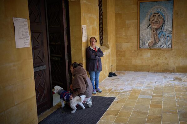 Католичка стоит на коленях рядом со своей собакой у входа в церковь во время мессы в Вербное воскресенье в Бейруте, Ливан. - Sputnik Казахстан