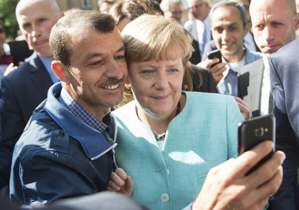 Беженец делает селфи с канцлером Германии Ангелой Меркель во время ее визита в центр для новоприбывших беженцев в Берлине - Sputnik Казахстан