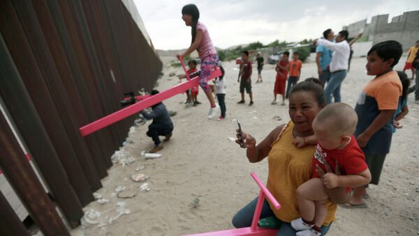 Дети играют на качелях, установленных между стальным забором, который отделяет Мексику от Соединенных Штатов в Сьюдад-де-Хуарес, Мексика - Sputnik Казахстан