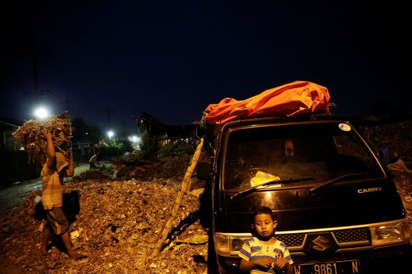 Ребенок ждет, пока взрослые занимаются погрузкой мусора в деревне Бангун в Индонезии - Sputnik Казахстан