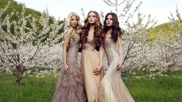 Три красивые девушки с длинными волосами и макияжем, одетые в вечерние платья, позируют в весеннем саду - Sputnik Казахстан