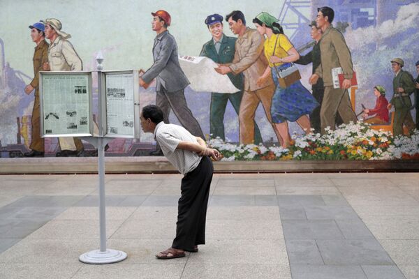 Пассажир метро в Пхеньяне читает газету на стенде - Sputnik Казахстан