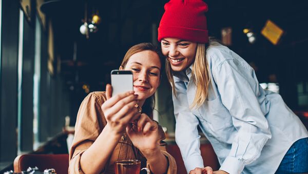 Две подруги смотрят смешные видео на смартфоне в кафе - Sputnik Казахстан
