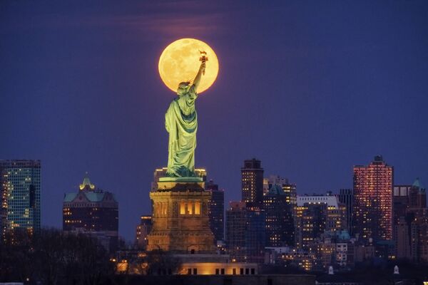The rising full moon crosses behind the Statue of Liberty, Monday evening, March 9, 2020, in New York City.  - Sputnik Казахстан
