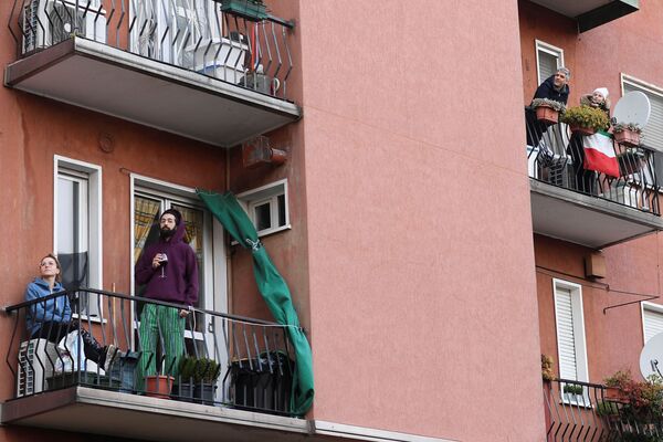 People listen to music as a neighbor plays the guitar and sings from a balcony to raise morale on the sixth day of an unprecedented lockdown across of all Italy imposed to slow the outbreak of coronavirus in Milan, Italy March 15, 2020. 
Люди на балконах во время карантина в Милане, Италия - Sputnik Казахстан