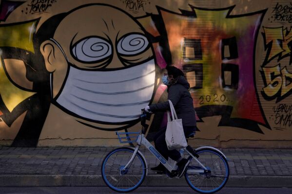 A woman wearing a protective mask cycles past graffiti-painted wall at a construction site in Shanghai, China, as the country is hit by coronavirus outbreak, February 17, 2020.  - Sputnik Казахстан