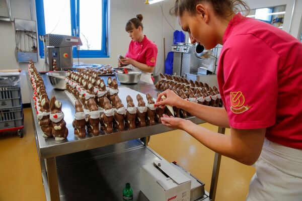 Работники готовят шоколадных пасхальных кроликов в защитных масках в пекарне Baeckerei Bohnenblust в Берне, Швейцария - Sputnik Казахстан