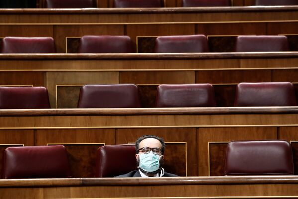 Spanish far-right Vox party's deputy Jose Maria Sanchez Garcia, wearing a face mask, sits in the almost empty Spanish parliament while the majority of lawmakers follow the session online as Spain's Prime Minister Pedro Sanchez explains measures under the state of emergency in Madrid, Spain, Wednesday March 18, 2020. Spain will mobilize 200 billion euros or the equivalent to one fifth of the country's annual output in loans, credit guarantees and subsidies for workers and vulnerable citizens Pedro Sanchez announced earlier. For most people, the new coronavirus causes only mild or moderate symptoms. For some, it can cause more severe illness, especially in older adults and people with existing health problems.  - Sputnik Казахстан