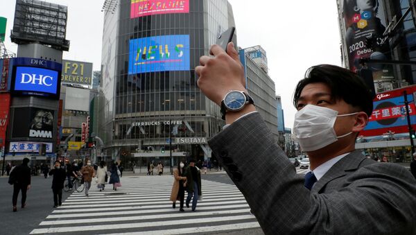 Мужчина в защитной маске фотографирует на мобильный телефон в полдень на перекрестке Сибуя в Токио во время пандемии коронавируса  - Sputnik Казахстан