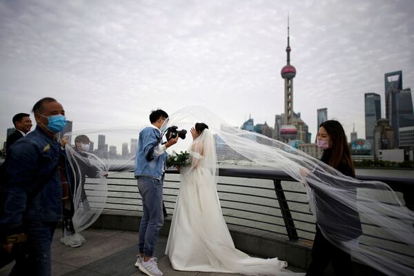 Staff members wearing face masks help a couple with their wedding photo shoot after the city's emergency alert level for coronavirus disease (COVID-19) was downgraded, on The Bund in Shanghai, China March 23, 2020.  - Sputnik Казахстан